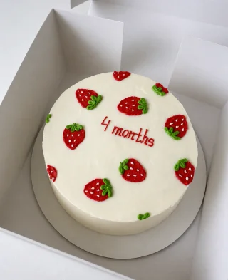 Білий торт з полуничками і написом «4 months» у коробці